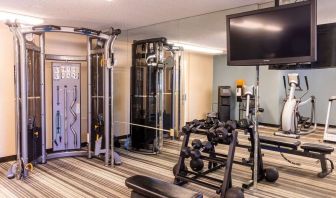 The hotel fitness center is equipped with assorted free weights, benches, a TV, and various exercise machines.