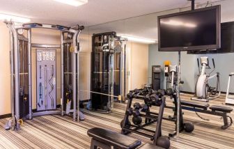 The hotel fitness center is equipped with assorted free weights, benches, a TV, and various exercise machines.