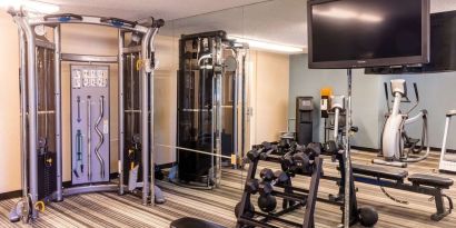 The hotel fitness center is equipped with assorted free weights, benches, a TV, and various exercise machines.