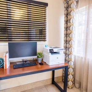 The hotel business center has a printer, monitor, keyboard, mouse, and a nearby window.