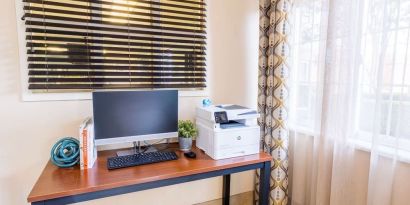 The hotel business center has a printer, monitor, keyboard, mouse, and a nearby window.