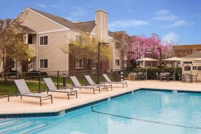 Shaded tables and chairs, as well as sun loungers, are by the side of Sonesta ES Suites Nashville Brentwood’s outdoor pool.