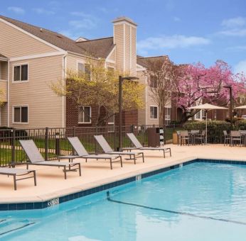 Shaded tables and chairs, as well as sun loungers, are by the side of Sonesta ES Suites Nashville Brentwood’s outdoor pool.