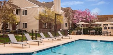 Shaded tables and chairs, as well as sun loungers, are by the side of Sonesta ES Suites Nashville Brentwood’s outdoor pool.