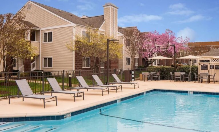 Shaded tables and chairs, as well as sun loungers, are by the side of Sonesta ES Suites Nashville Brentwood’s outdoor pool.