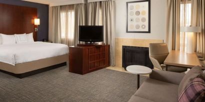 Sonesta ES Suites Nashville Brentwood king bed guest room, furnished with sofa, desk, and TV.