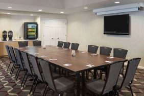 Hotel meeting room, including a long wooden table, projector screen, wall-mounted TV, and seating for over a dozen attendees.