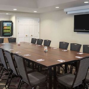 Hotel meeting room, including a long wooden table, projector screen, wall-mounted TV, and seating for over a dozen attendees.