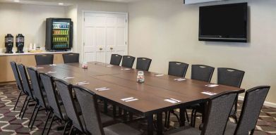 Hotel meeting room, including a long wooden table, projector screen, wall-mounted TV, and seating for over a dozen attendees.