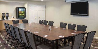 Hotel meeting room, including a long wooden table, projector screen, wall-mounted TV, and seating for over a dozen attendees.