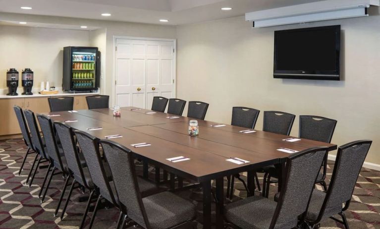 Hotel meeting room, including a long wooden table, projector screen, wall-mounted TV, and seating for over a dozen attendees.