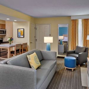 Sonesta ES Suites Cincinnati - Blue Ash guest room lounge, with armchair, sofa, and television, plus nearby kitchenette.