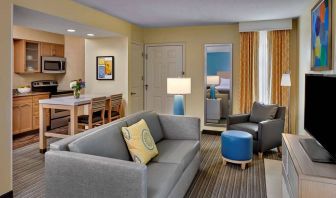 Sonesta ES Suites Cincinnati - Blue Ash guest room lounge, with armchair, sofa, and television, plus nearby kitchenette.