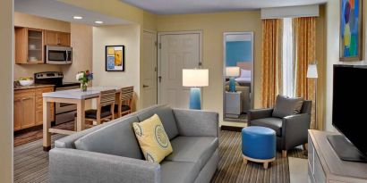 Sonesta ES Suites Cincinnati - Blue Ash guest room lounge, with armchair, sofa, and television, plus nearby kitchenette.