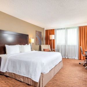 Double bed guest room in Sonesta Miami Airport, including armchair, TV, and window.