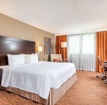 Double bed guest room in Sonesta Miami Airport, including armchair, TV, and window.