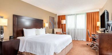 Double bed guest room in Sonesta Miami Airport, including armchair, TV, and window.