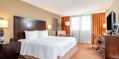 Double bed guest room in Sonesta Miami Airport, including armchair, TV, and window.