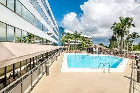 Sonesta Miami Airport’s outdoor pool has palm trees nearby, with tables and chairs, and sun loungers, by the side.