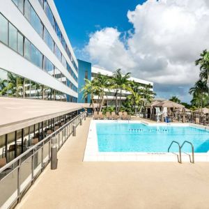 Sonesta Miami Airport’s outdoor pool has palm trees nearby, with tables and chairs, and sun loungers, by the side.