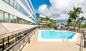 Sonesta Miami Airport’s outdoor pool has palm trees nearby, with tables and chairs, and sun loungers, by the side.