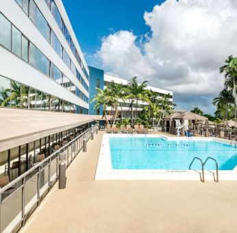 Sonesta Miami Airport’s outdoor pool has palm trees nearby, with tables and chairs, and sun loungers, by the side.