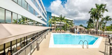 Sonesta Miami Airport’s outdoor pool has palm trees nearby, with tables and chairs, and sun loungers, by the side.