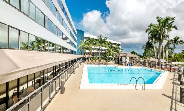 Sonesta Miami Airport’s outdoor pool has palm trees nearby, with tables and chairs, and sun loungers, by the side.