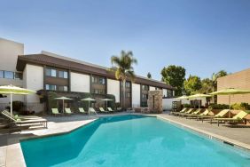 The outdoor pool of Sonesta Silicon Valley has nearby sun loungers, tables and chairs, and plenty of shade available.