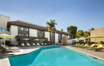The outdoor pool of Sonesta Silicon Valley has nearby sun loungers, tables and chairs, and plenty of shade available.