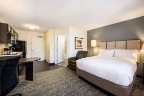 Sonesta Simply Suites Cleveland North Olmsted Airport double bed guest room, featuring armchair, desk, and kitchenette.