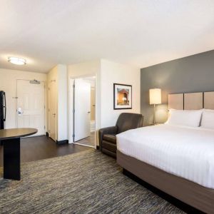 Sonesta Simply Suites Cleveland North Olmsted Airport double bed guest room, featuring armchair, desk, and kitchenette.