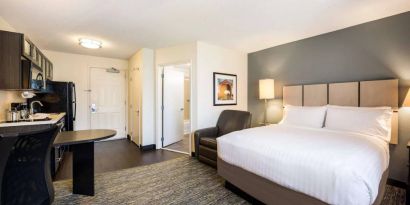 Sonesta Simply Suites Cleveland North Olmsted Airport double bed guest room, featuring armchair, desk, and kitchenette.