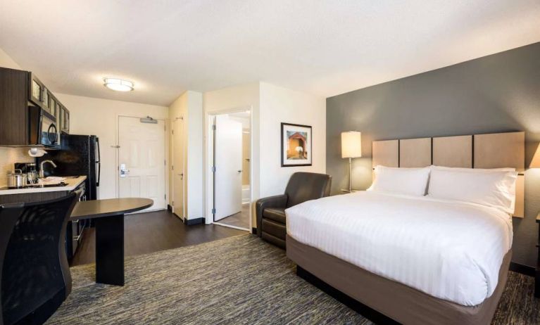 Sonesta Simply Suites Cleveland North Olmsted Airport double bed guest room, featuring armchair, desk, and kitchenette.