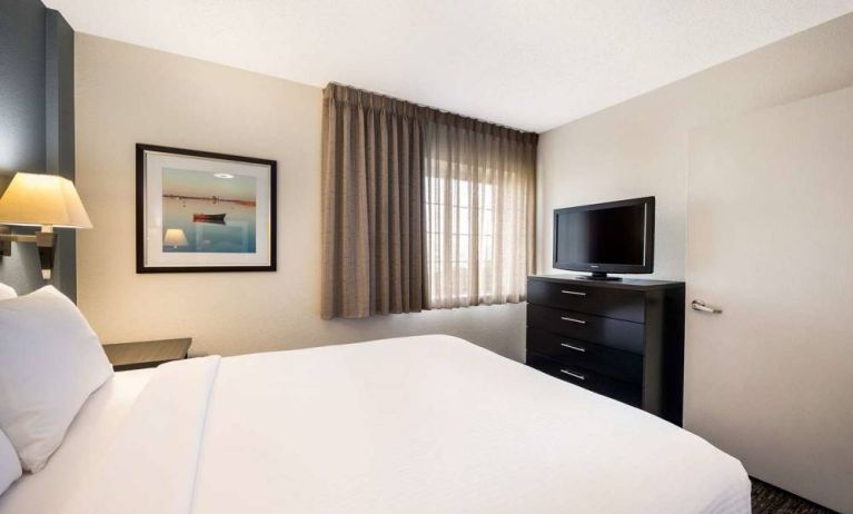 Sonesta Simply Suites Baltimore BWI Airport double bed guest room, featuring window, bedside lamp, and television.