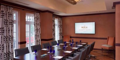 The Stephen F Austin Royal Sonesta Hotel meeting room, with long wooden table, ten swivel chairs, and wall-mounted television.