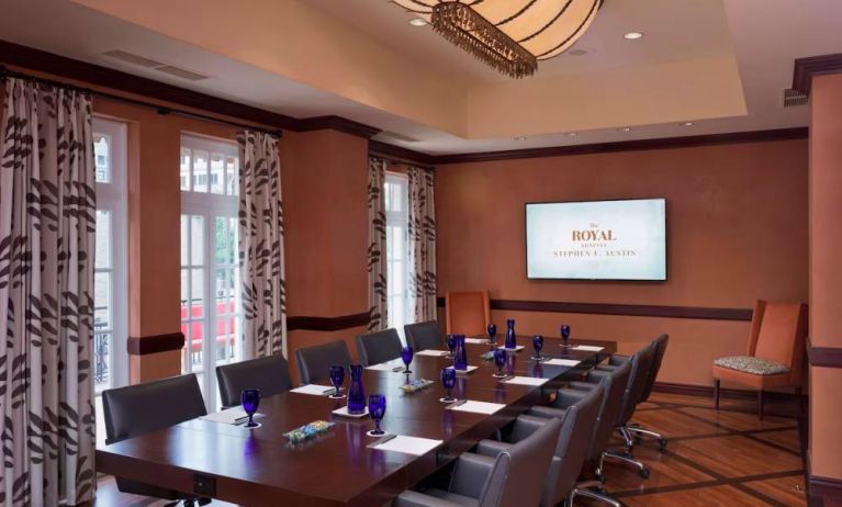 The Stephen F Austin Royal Sonesta Hotel meeting room, with long wooden table, ten swivel chairs, and wall-mounted television.