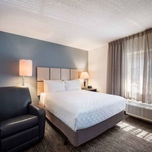 Double bed guest room in Sonesta Simply Suites Nashville Brentwood, featuring armchair, bedside lamp, and window.