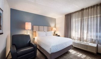 Double bed guest room in Sonesta Simply Suites Nashville Brentwood, featuring armchair, bedside lamp, and window.