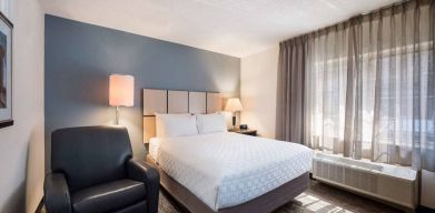 Double bed guest room in Sonesta Simply Suites Nashville Brentwood, featuring armchair, bedside lamp, and window.