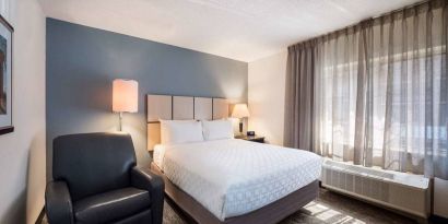 Double bed guest room in Sonesta Simply Suites Nashville Brentwood, featuring armchair, bedside lamp, and window.