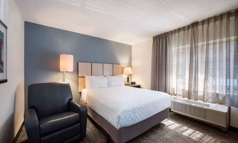 Double bed guest room in Sonesta Simply Suites Nashville Brentwood, featuring armchair, bedside lamp, and window.