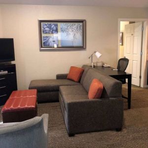 Sonesta ES Suites San Jose Airport guest room lounge with TV, sofa, and armchair, with adjacent workspace area.