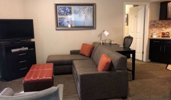 Sonesta ES Suites San Jose Airport guest room lounge with TV, sofa, and armchair, with adjacent workspace area.