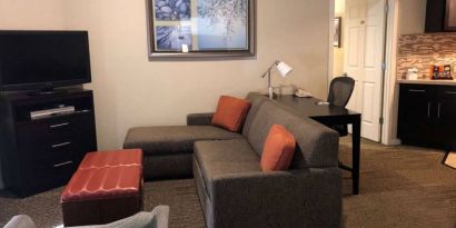 Sonesta ES Suites San Jose Airport guest room lounge with TV, sofa, and armchair, with adjacent workspace area.