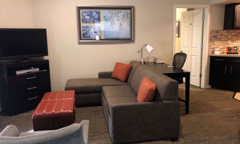 Sonesta ES Suites San Jose Airport guest room lounge with TV, sofa, and armchair, with adjacent workspace area.