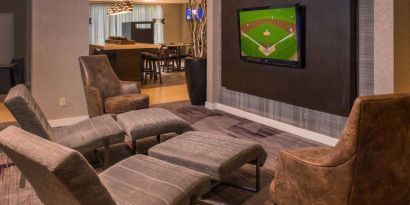 Sonesta Select Arlington Rosslyn’s lobby features a large, wall-mounted TV, with armchairs and reclined seating with footstools.