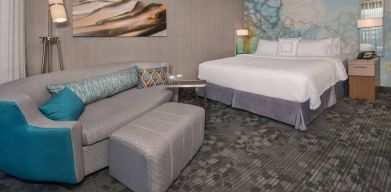 Sonesta Select Allentown Bethlehem Airport double bed guest room, with art on the wall, sofa, and long footstool.