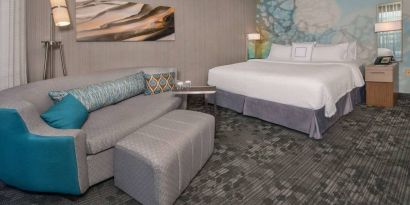 Sonesta Select Allentown Bethlehem Airport double bed guest room, with art on the wall, sofa, and long footstool.