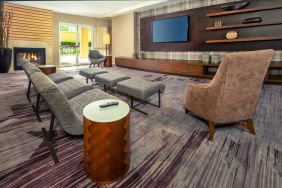 The hotel lobby is furnished with a very large TV, comfortable seating with footstools, a fireplace, and coffee tables.